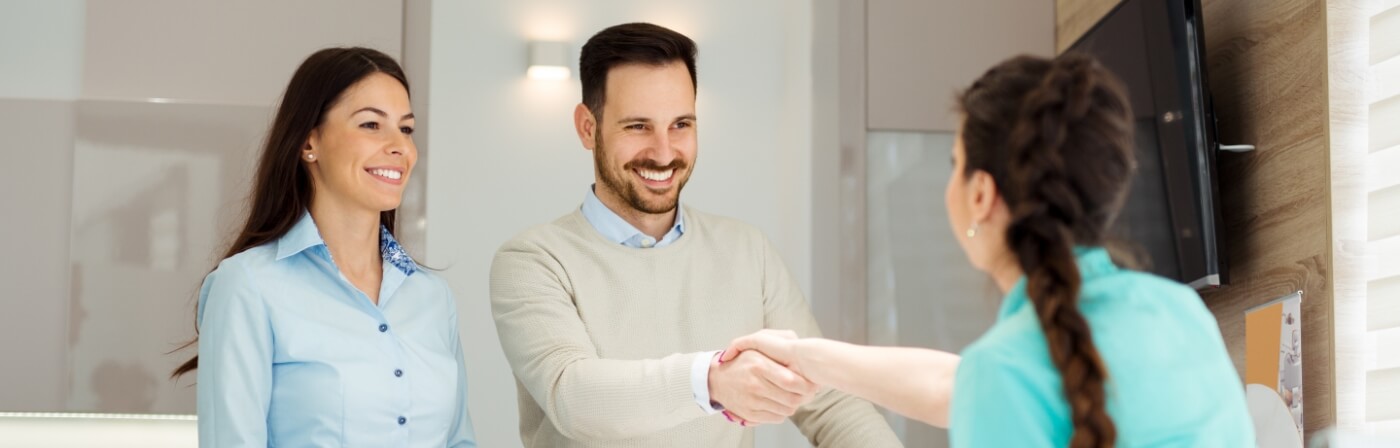 Smiling dental team member shaking hands with a patient at front desk