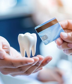 A hand holding a credit card to a dentist’s hands holding a levitating model tooth