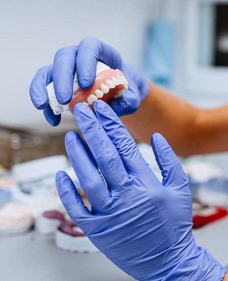 Dentist with blue gloves holding denture