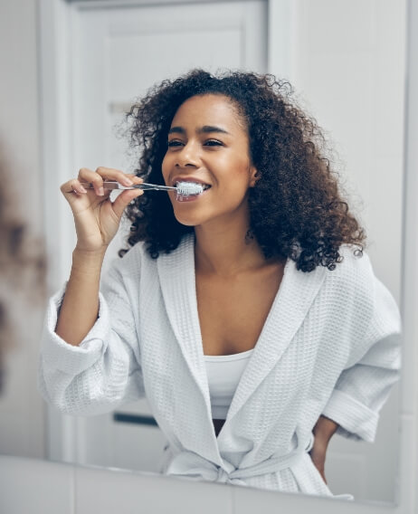 Woman in white bathrobe brushing her teeth