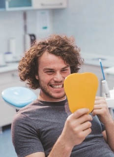 Young man in dental chair looking at his smile in a mirror