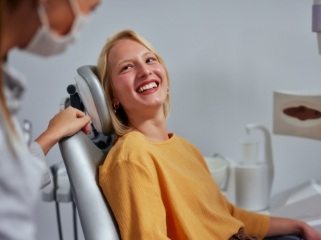 Woman in yellow sweater smiling in dental chair