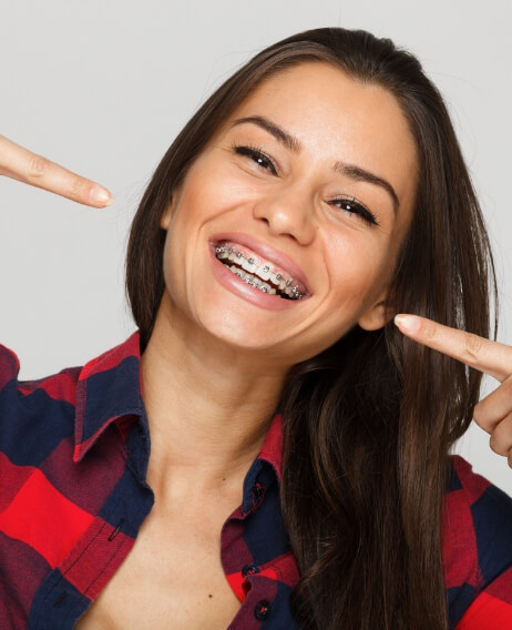 Young woman with traditional braces pointing to her smile