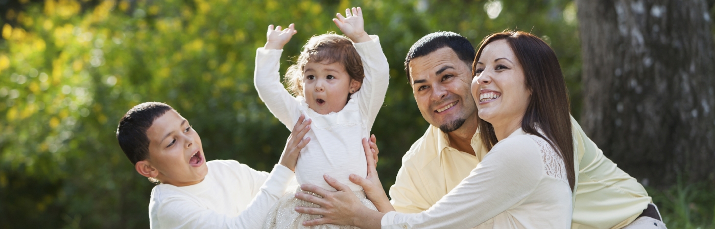 Family of four laughing together outdoors on sunny day