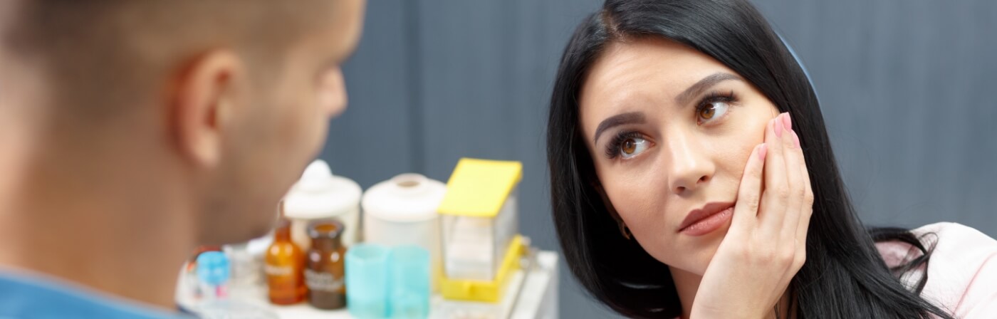 Woman holding her cheek in pain while talking to dentist about root canal treatment