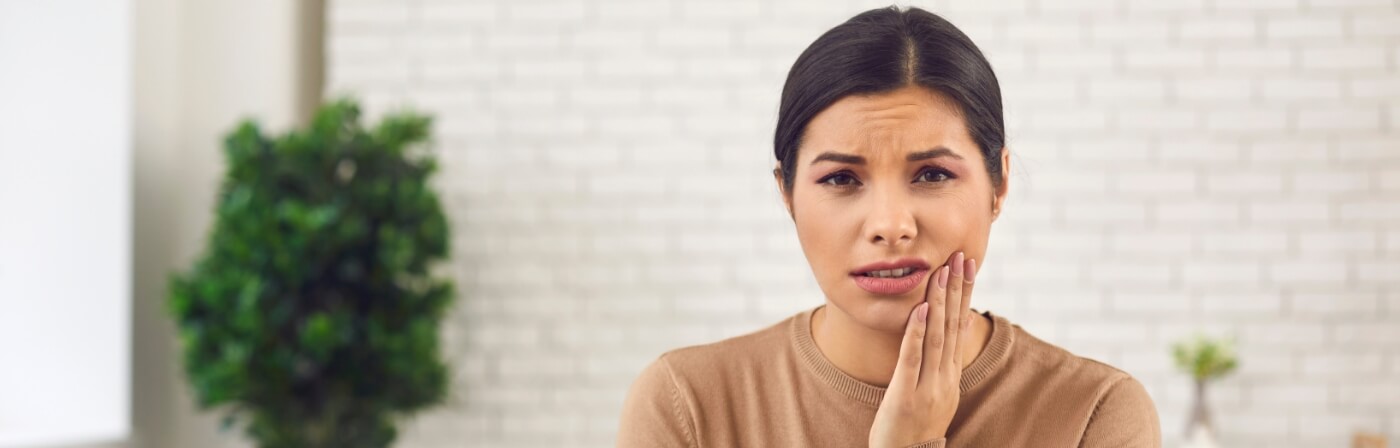 Woman holding her cheek in pain before wisdom tooth extractions in Dallas